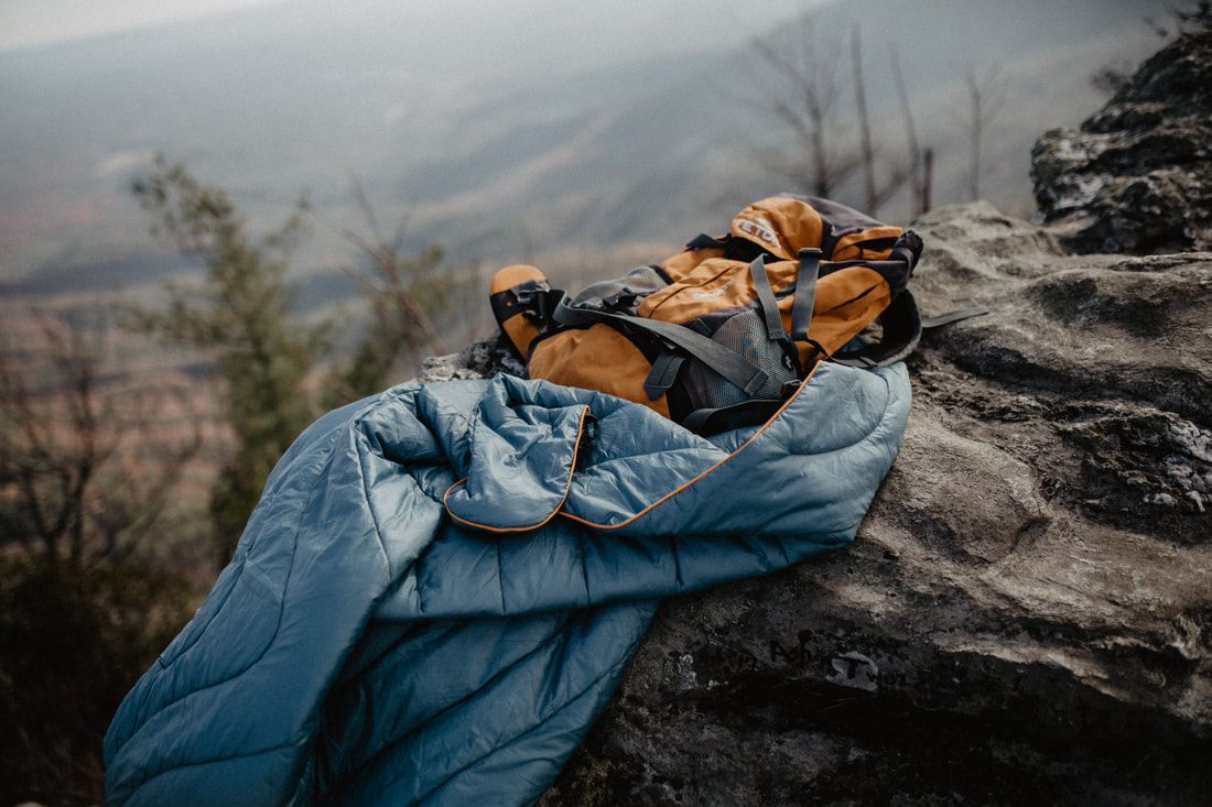 Person relaxing under a Rumpl blanket in a natural outdoor setting for a brand campaign.
