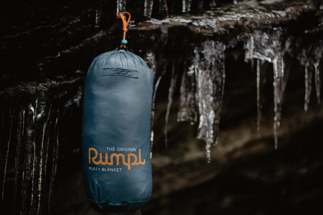 Person wrapped in a Rumpl travel blanket during an outdoor camping scene.