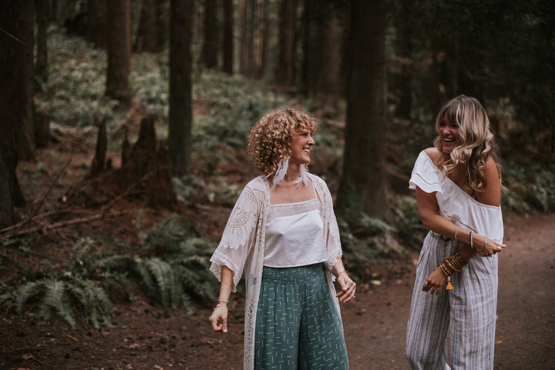 Two women posing confidently among lush PNW forest greenery