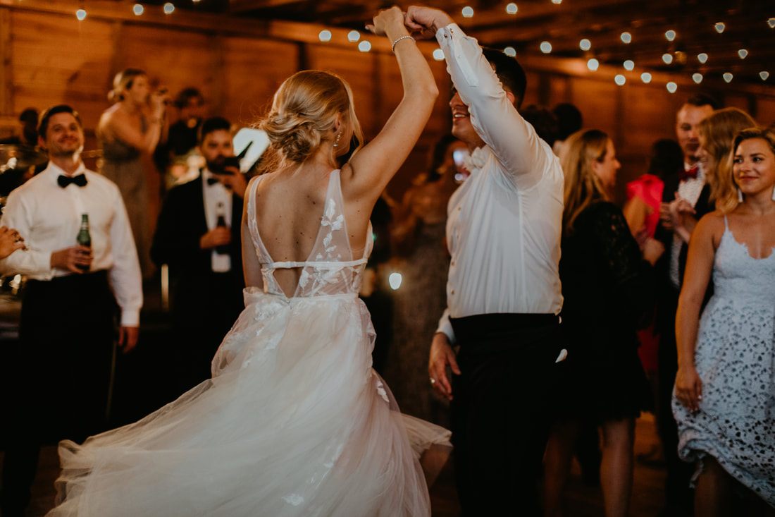 The newlyweds walking hand in hand under string lights at the barn
