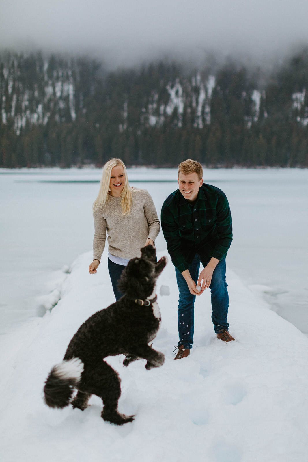 Couple standing in front of a wooden a-frame cabin surrounded by pine trees