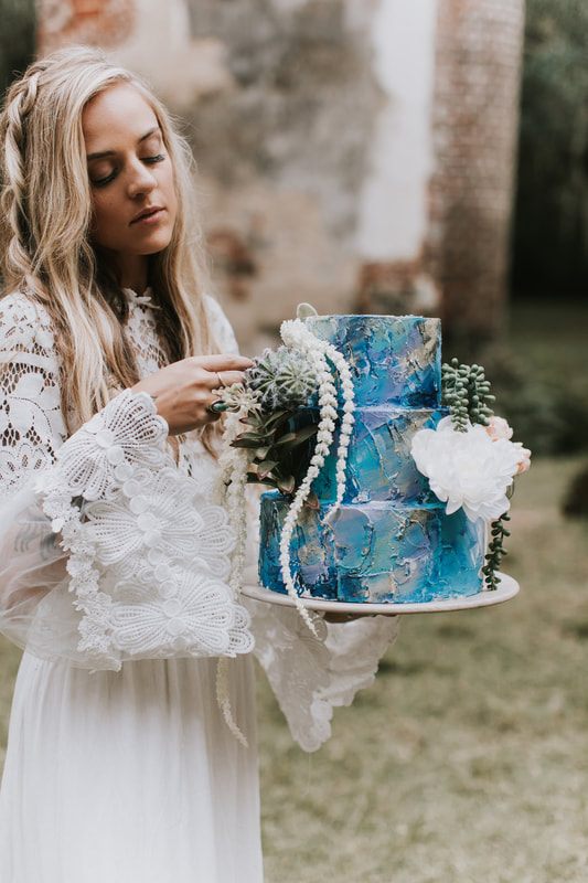 Bride and hand-painted cake styled together with dark floral and succulent accents.