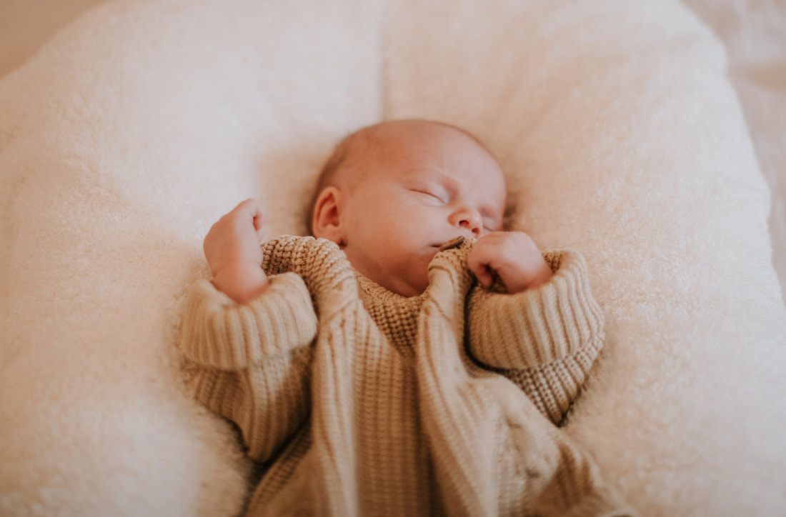 Newborn baby yawning while swaddled on a soft blanket