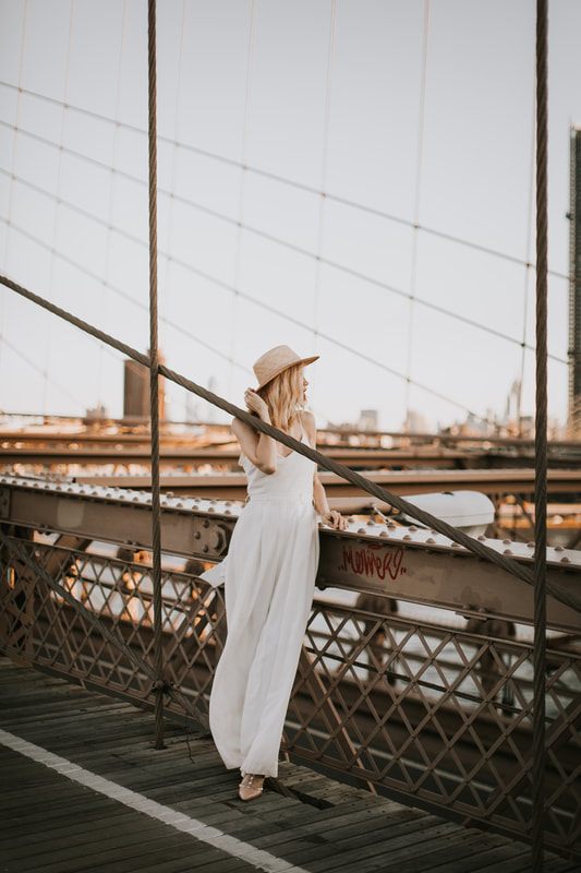 Valentina leaning against a Brooklyn storefront in her bridal romper