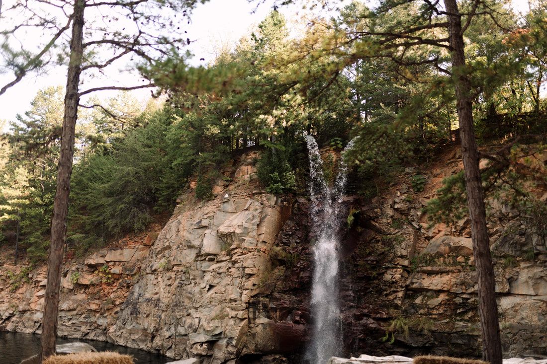 Couple holding hands while crossing rocks near the waterfall