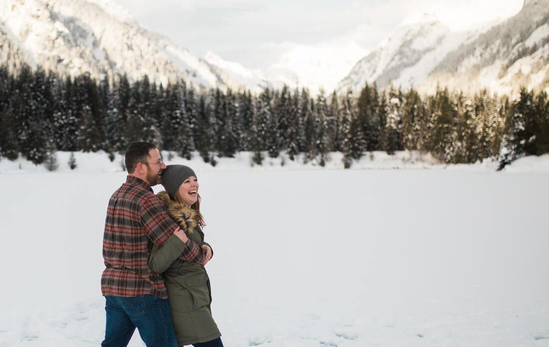 Couple standing at the edge of a snow-dusted mountain lake at golden hour