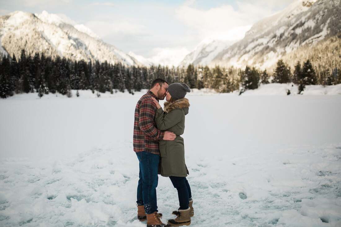 Engaged couple snowshoeing through snow-covered pines near Snoqualmie, Washington
