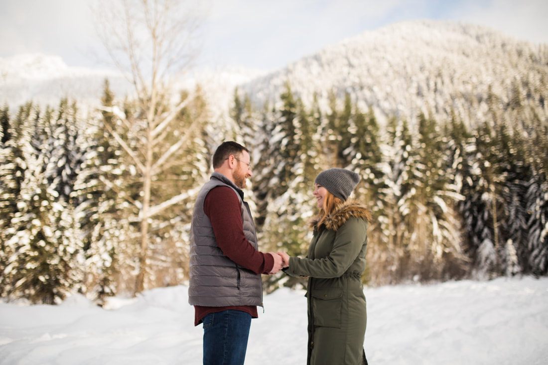 Engaged couple sharing a quiet moment among snow-covered evergreen trees