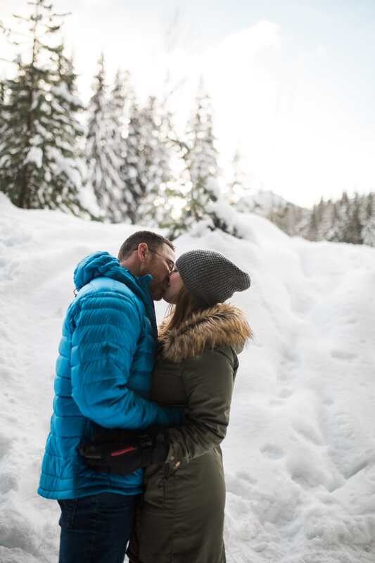 Engaged couple sitting together on a snowy log during their mountain photo session