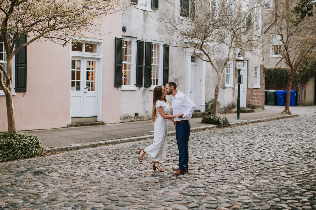 Engaged couple walking hand in hand down cobblestone Chalmers Street in Charleston