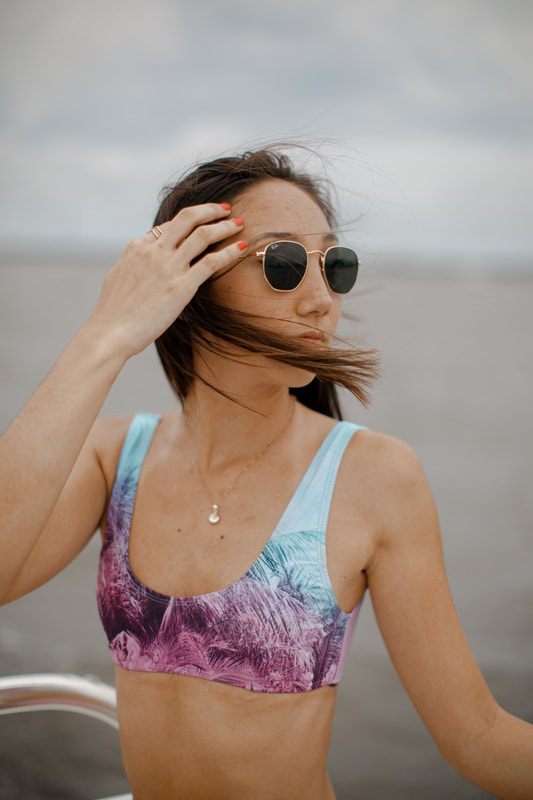 A swimwear model posing against a beach backdrop with a relaxed, sun-soaked feel