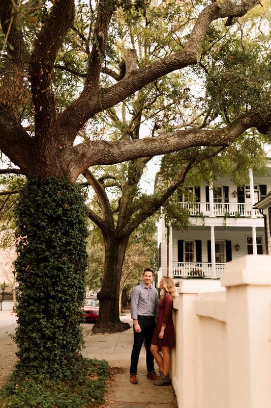 Wide shot of the couple walking past pastel row houses in downtown Charleston
