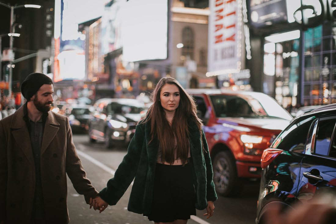 Engaged couple laughing together under New York City lights
