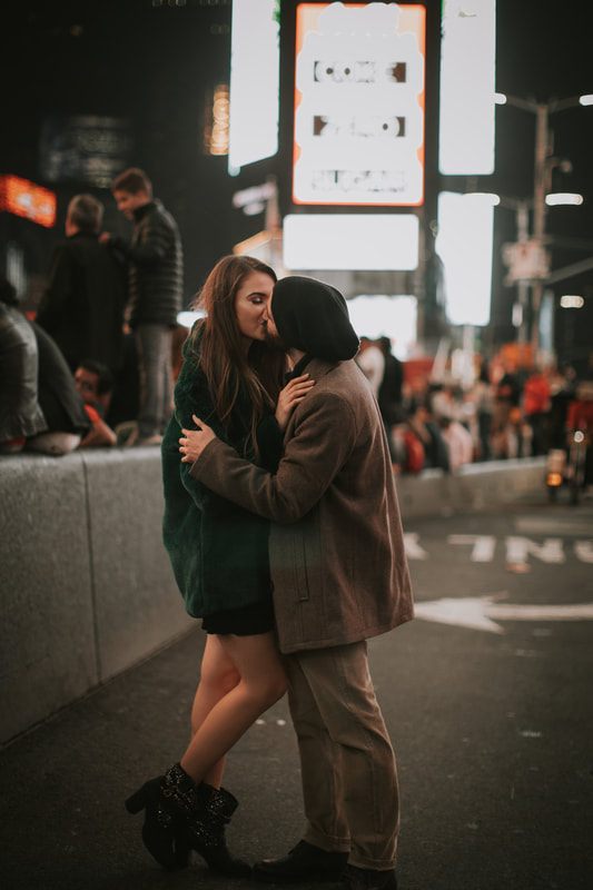 Engaged couple portrait with New York City lights glowing behind them