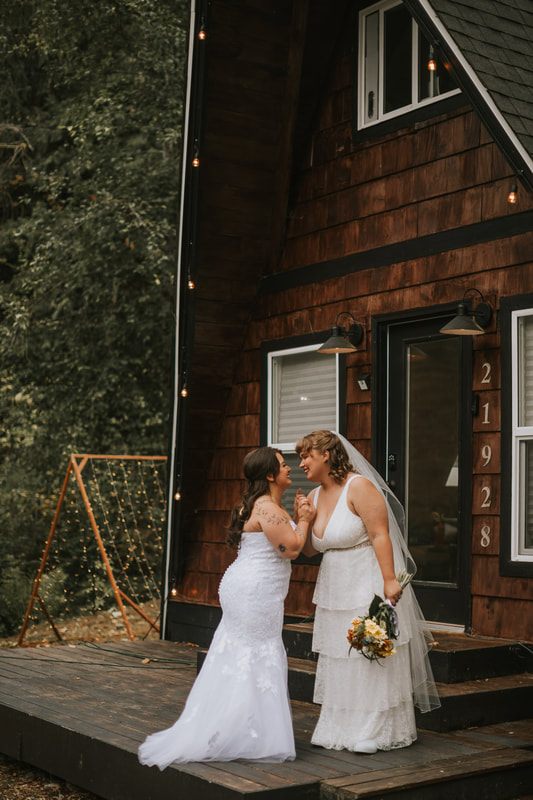 Two brides embracing on the porch of a Washington A-frame cabin, later in the celebration