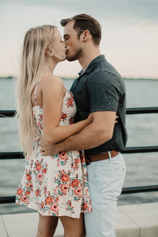 The engaged couple smiling at each other near a wrought-iron gate downtown