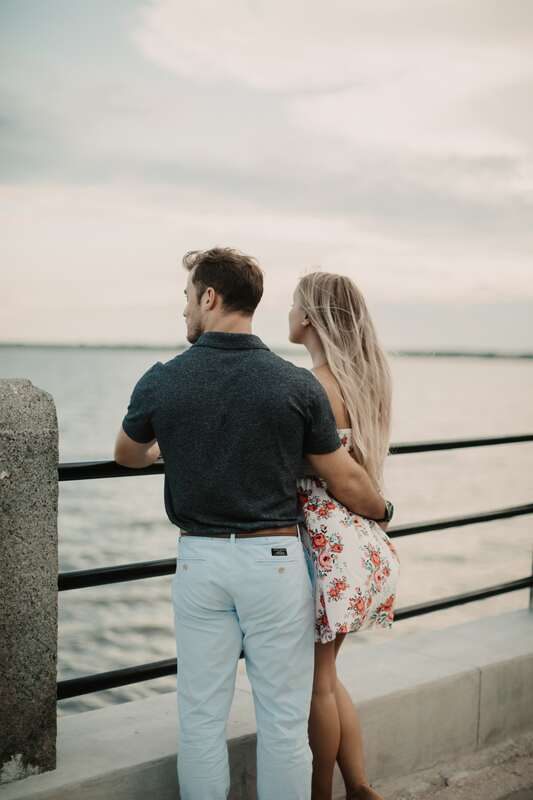 The couple walking hand in hand near a wrought-iron gate downtown