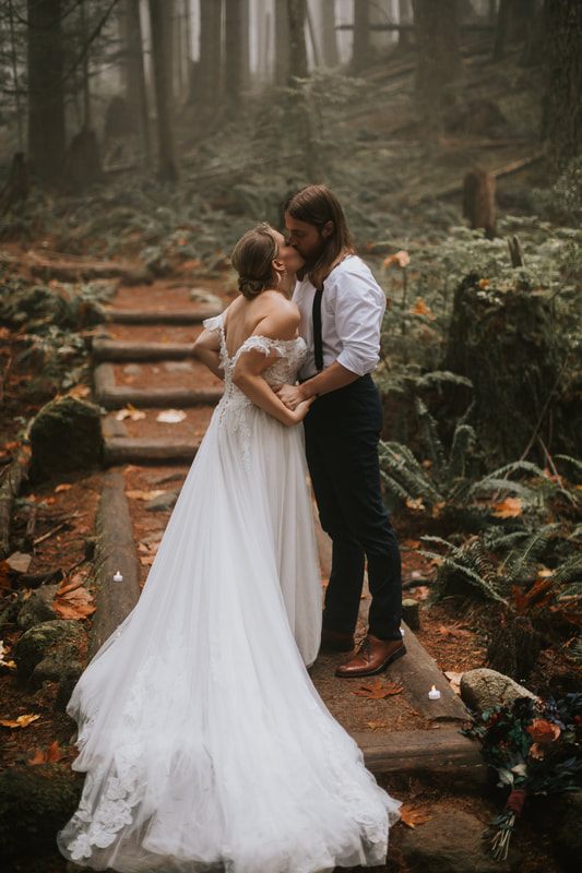 Bride's gown and bouquet detail against the moody, foggy forest backdrop.