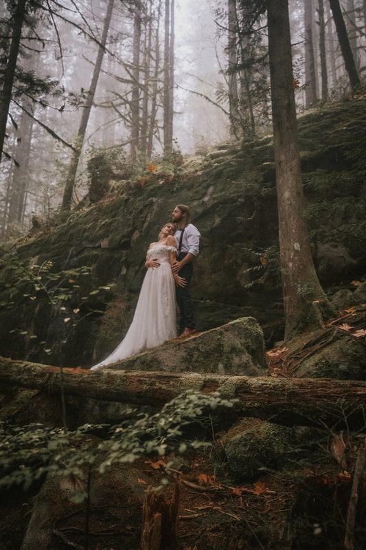 Bride and groom embracing beneath the fog-laced trees during their ceremony.