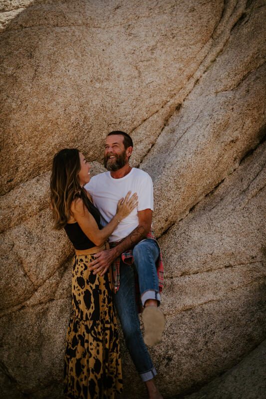 The couple laughing together against the vast desert landscape, from later in the session