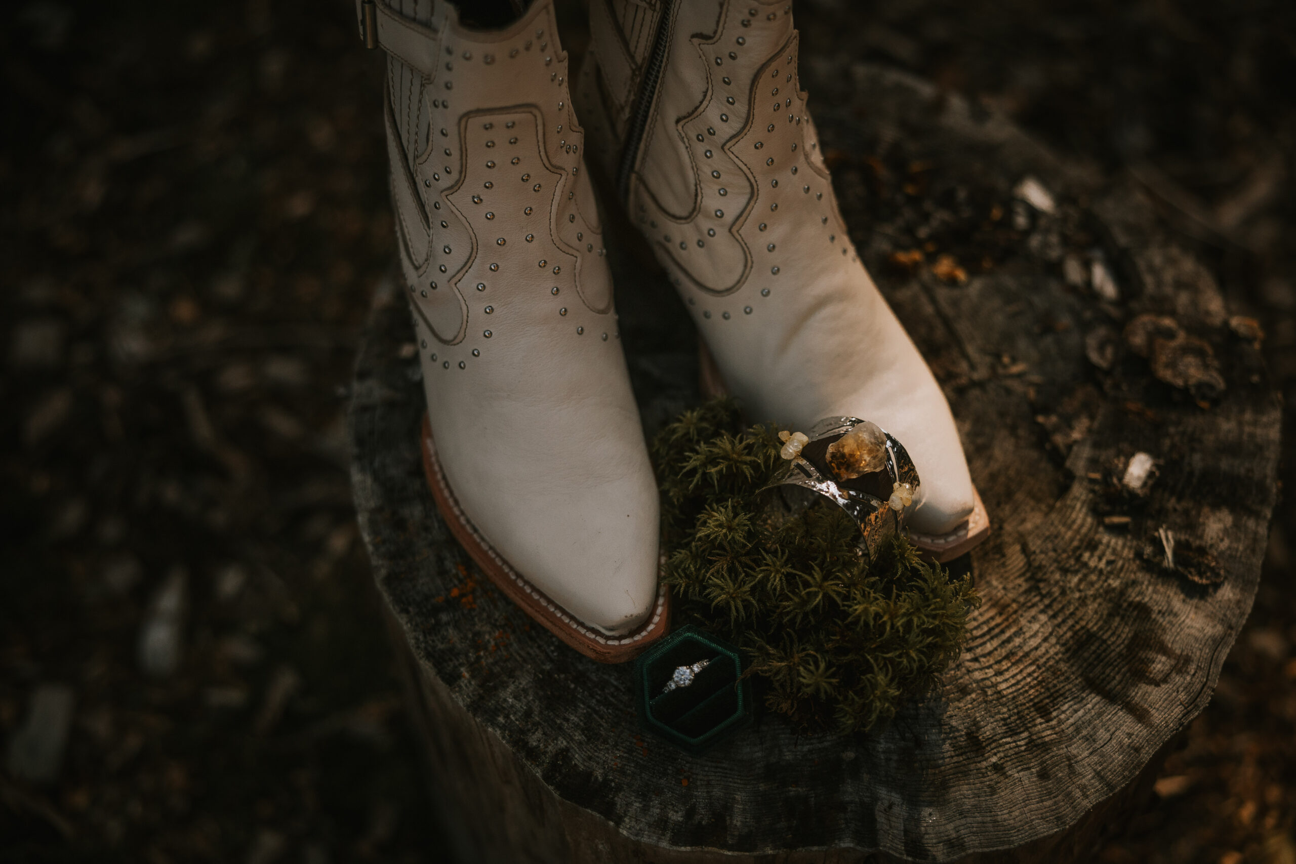 Justine's cream cowboy boots on a mossy tree stump with the wedding rings beside them