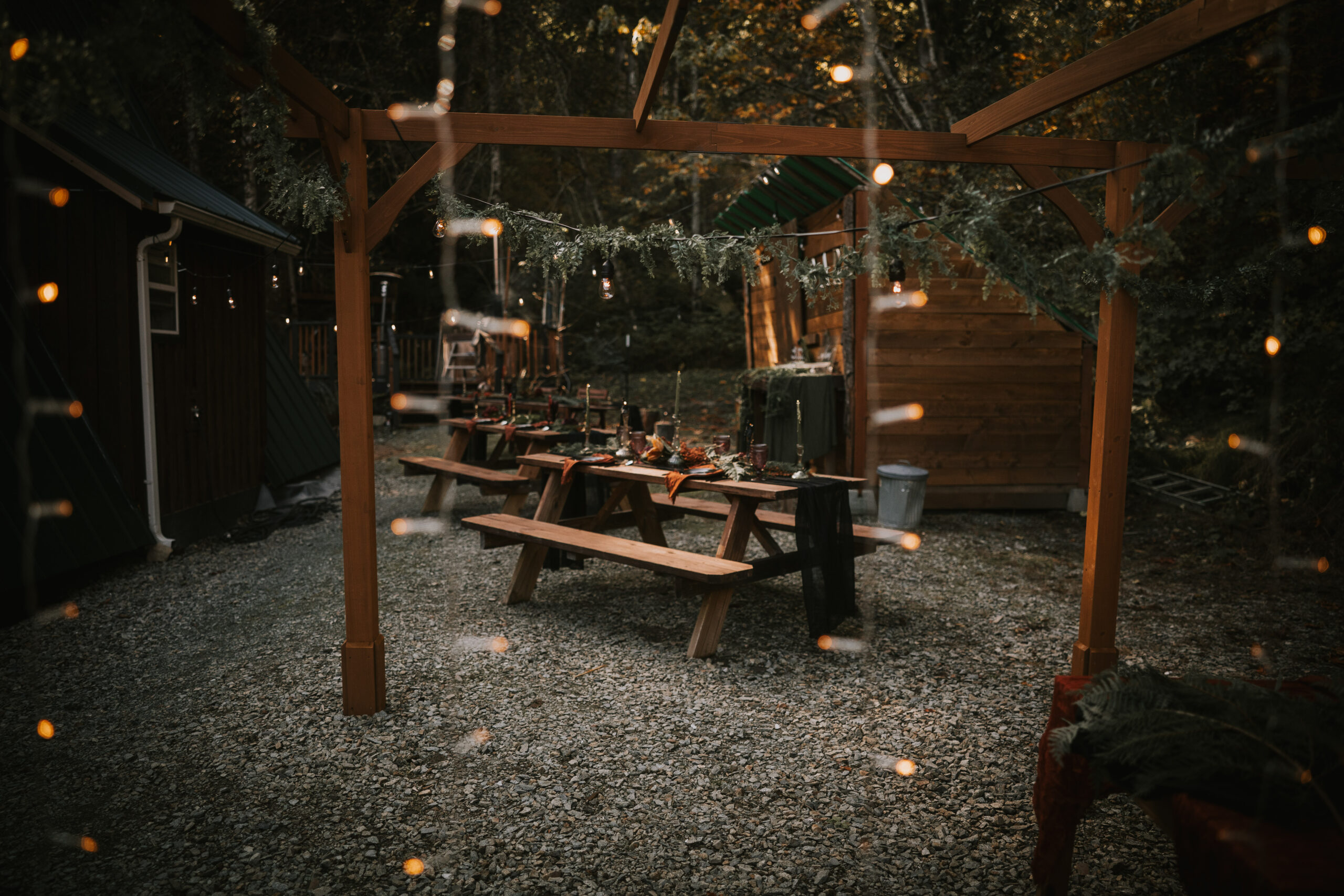 String lights over picnic tables set for dinner in the clearing at That PNW Cabin