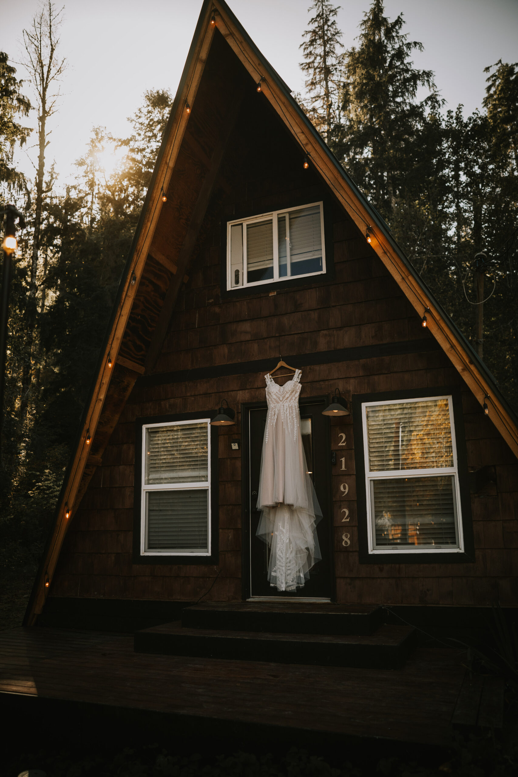 Justine's wedding dress hanging on the front of the A-frame at That PNW Cabin under string lights