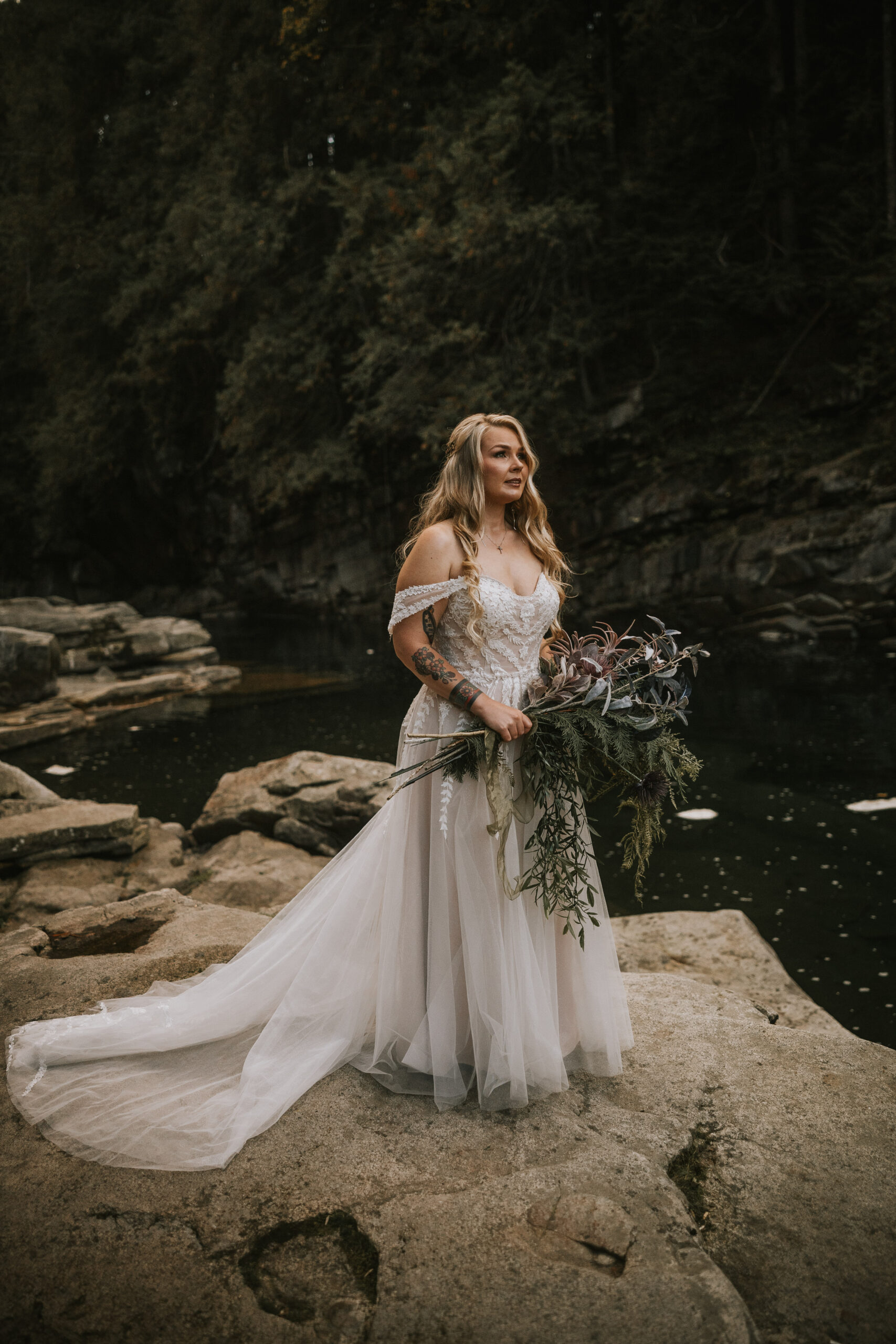 Justine standing on river rocks holding a large dried and foraged bouquet