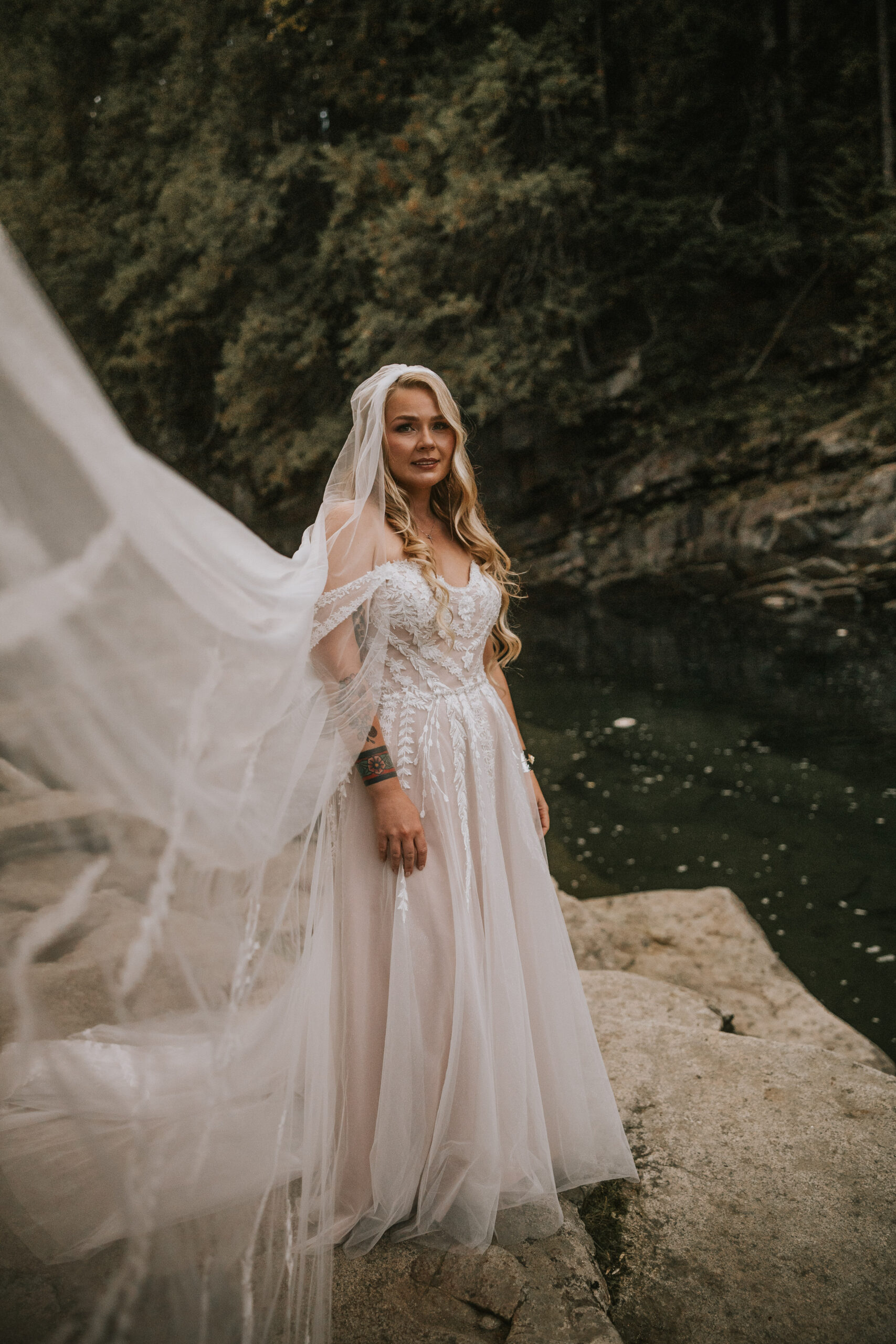 Justine on a boulder above the river with her long veil catching the wind