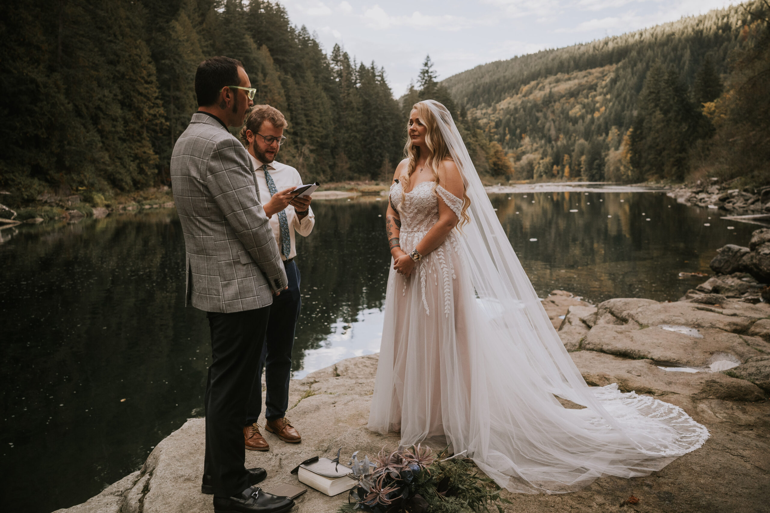 Justine laughing during the ceremony as the officiant reads, the lake behind them