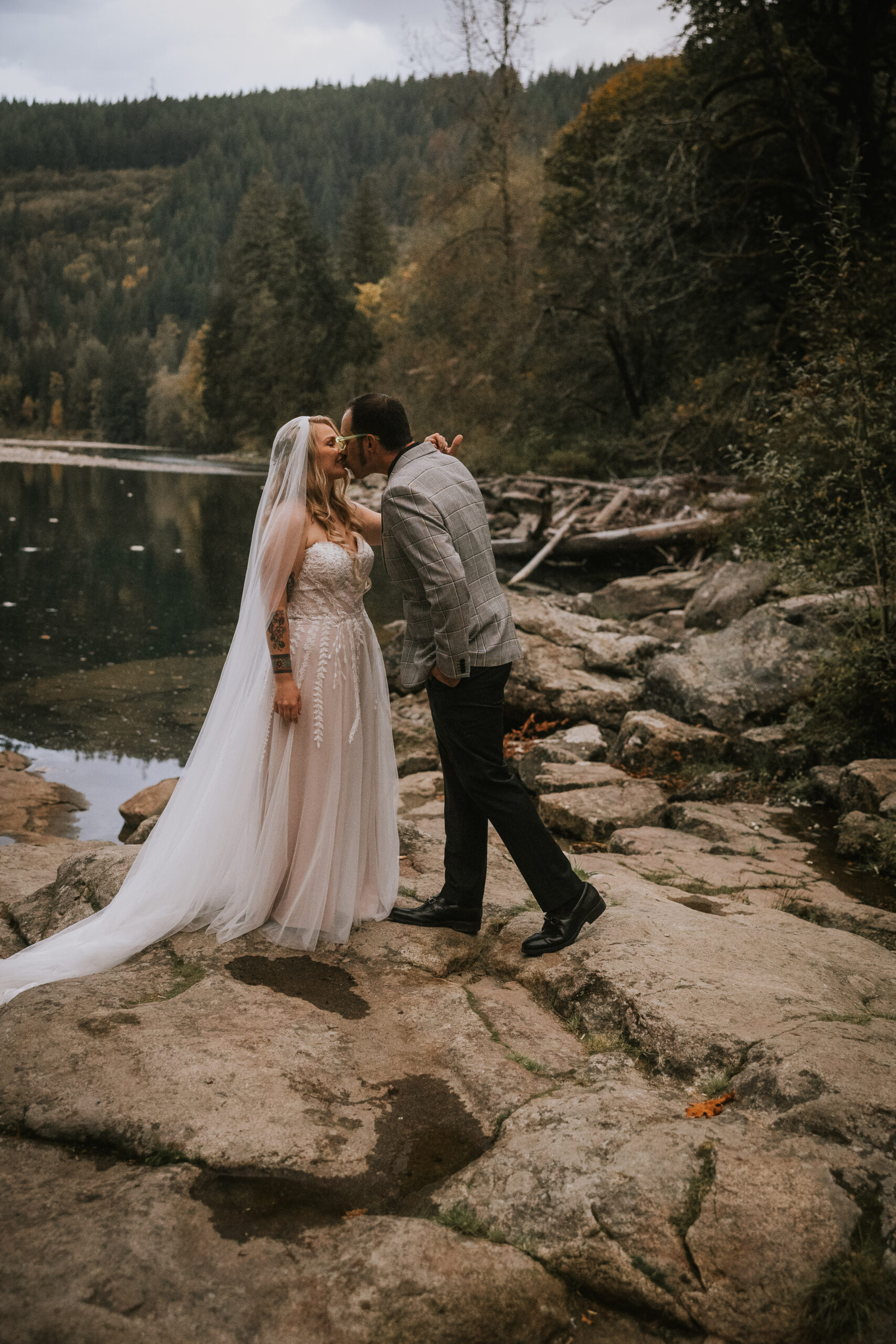 Justine and Zack kissing on the river rocks with autumn color in the trees behind
