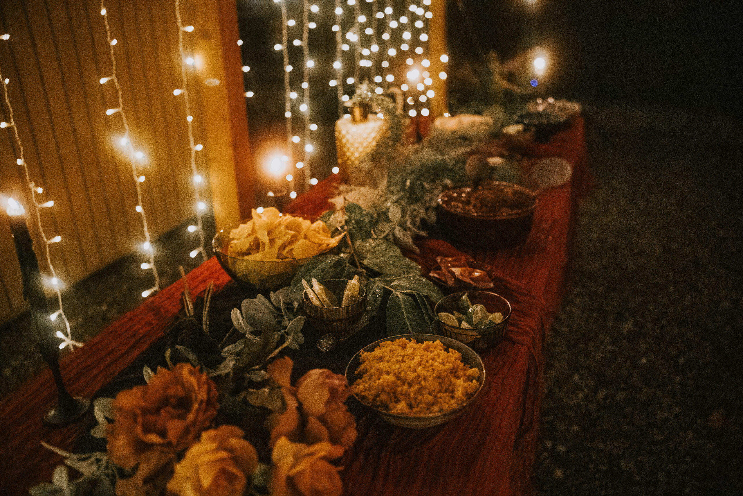 The food table at night lined with bowls and lit by curtain lights