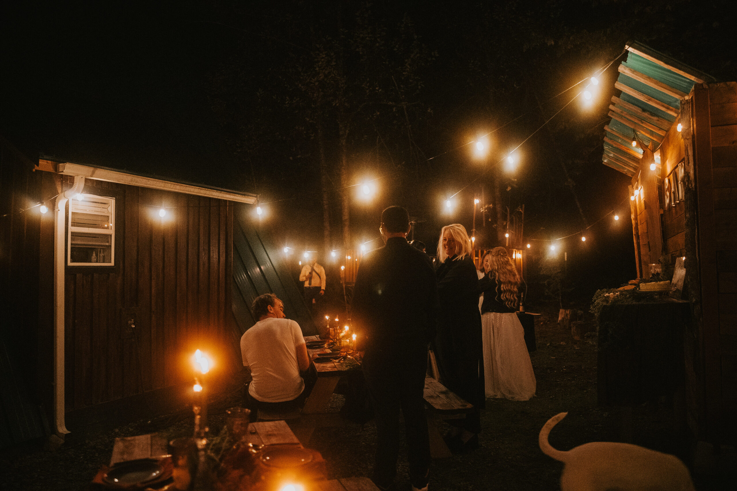 Guests standing and talking under string lights outside the cabin at night