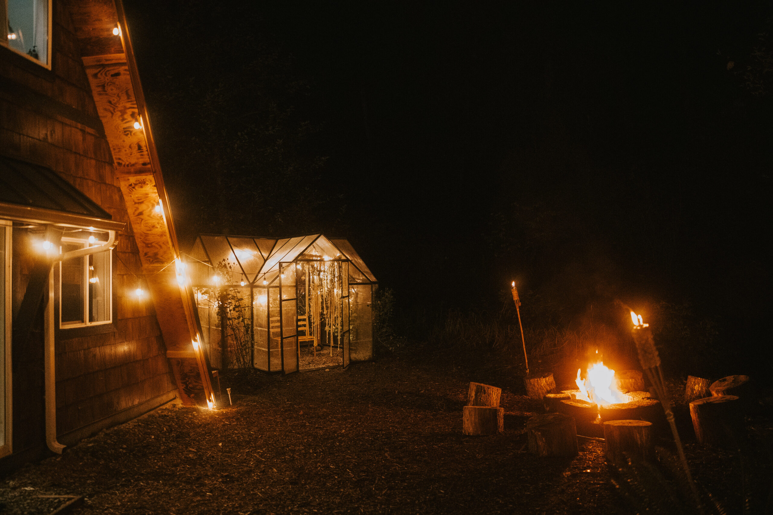 The greenhouse and the bonfire lit up beside the cabin at night