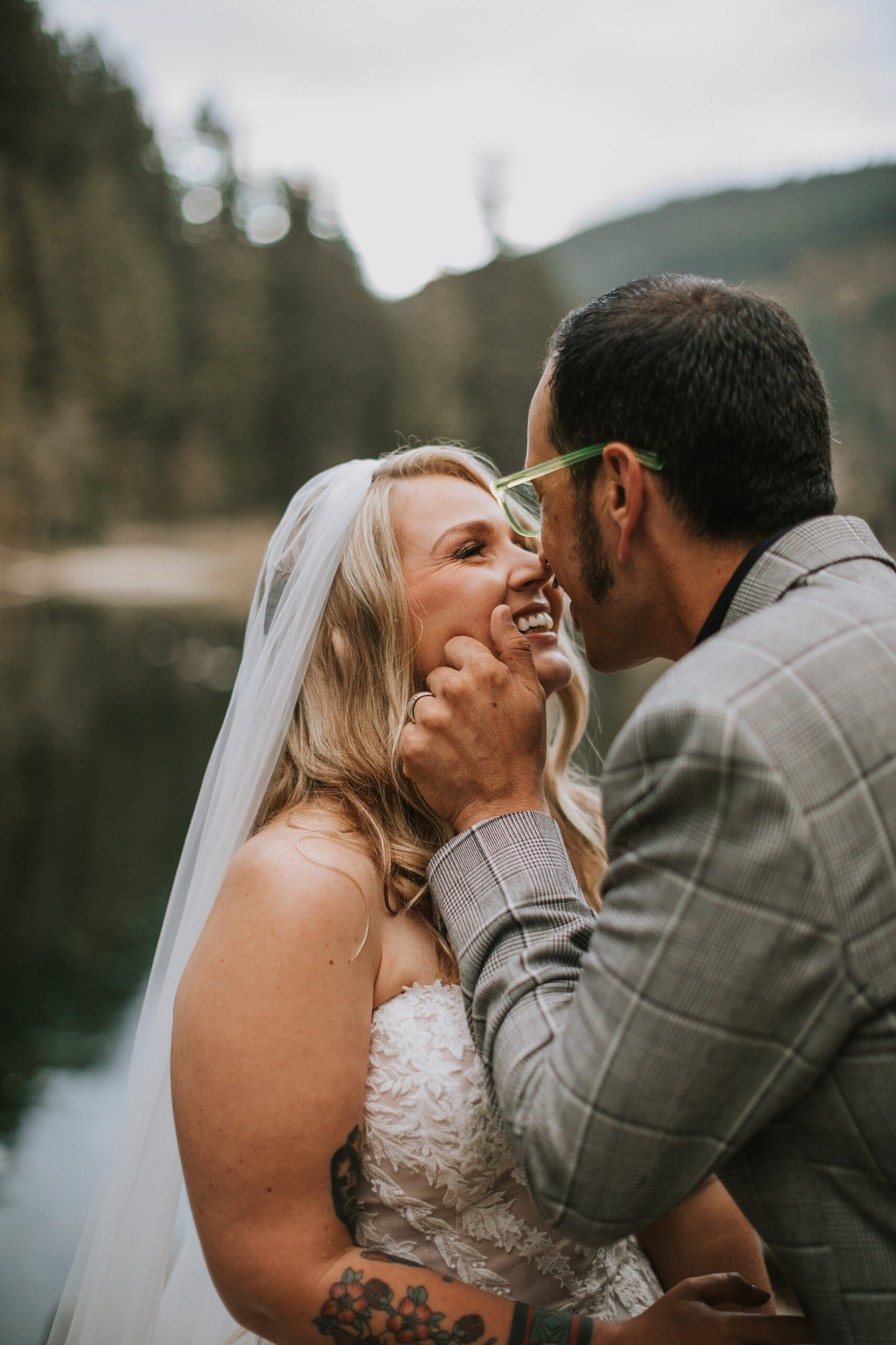 Zack cupping Justine's face as they both laugh, the lake blurred behind them