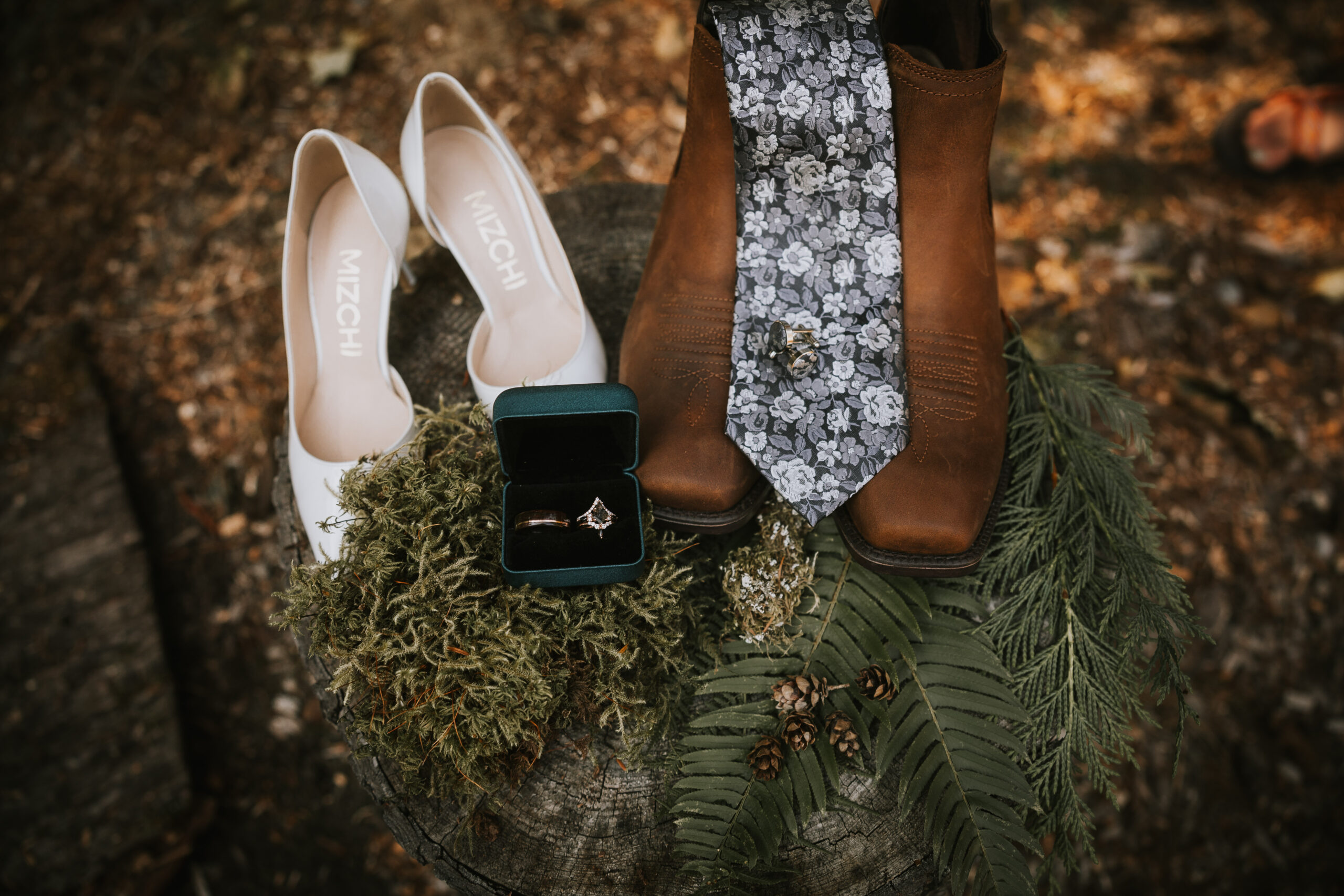 Detail of the wedding shoes, boots, tie and ring box arranged on moss and ferns