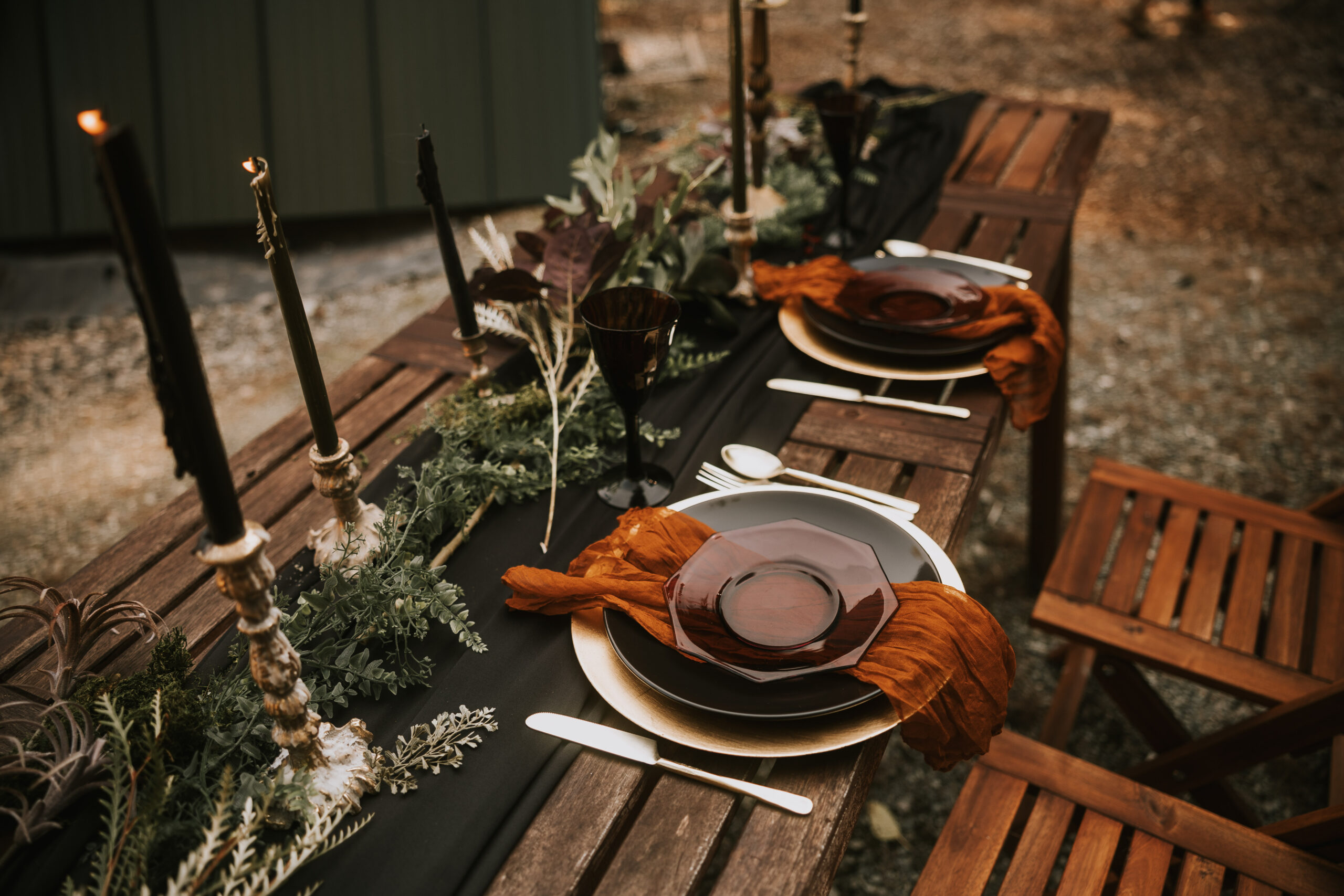 Table detail with a black runner, rust napkins, amber glassware and taper candles