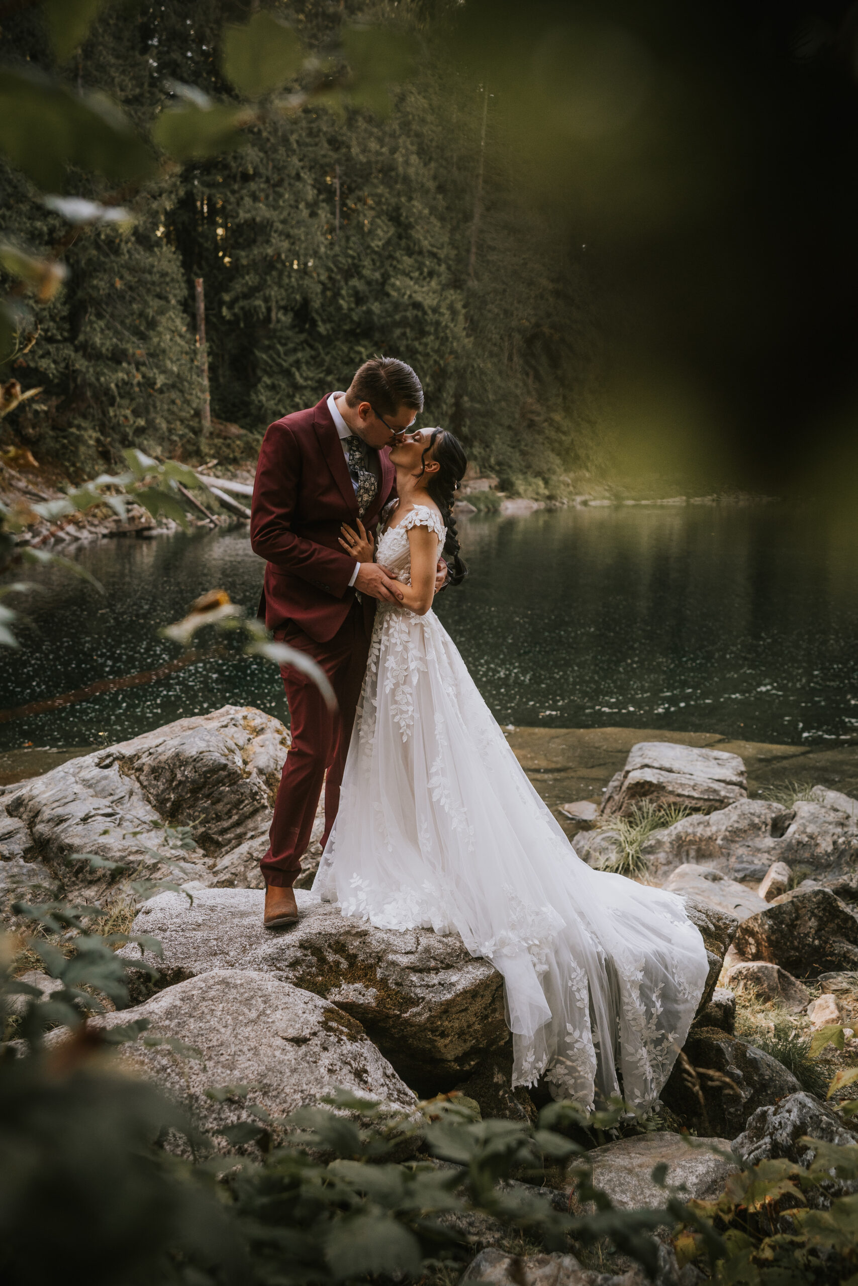Brandon and Morgan kissing on the rocks above the river, framed by leaves