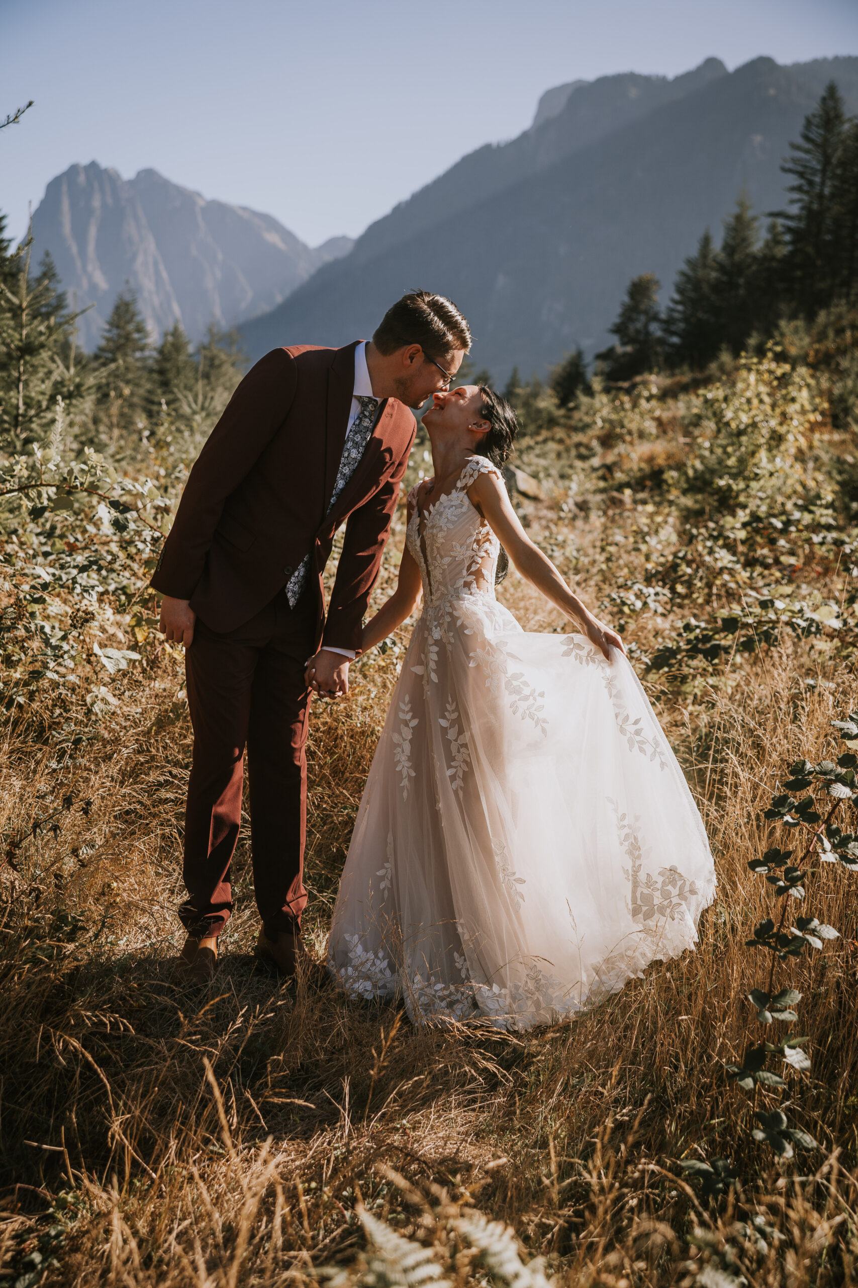 The couple kissing in a golden meadow with the mountains rising behind them