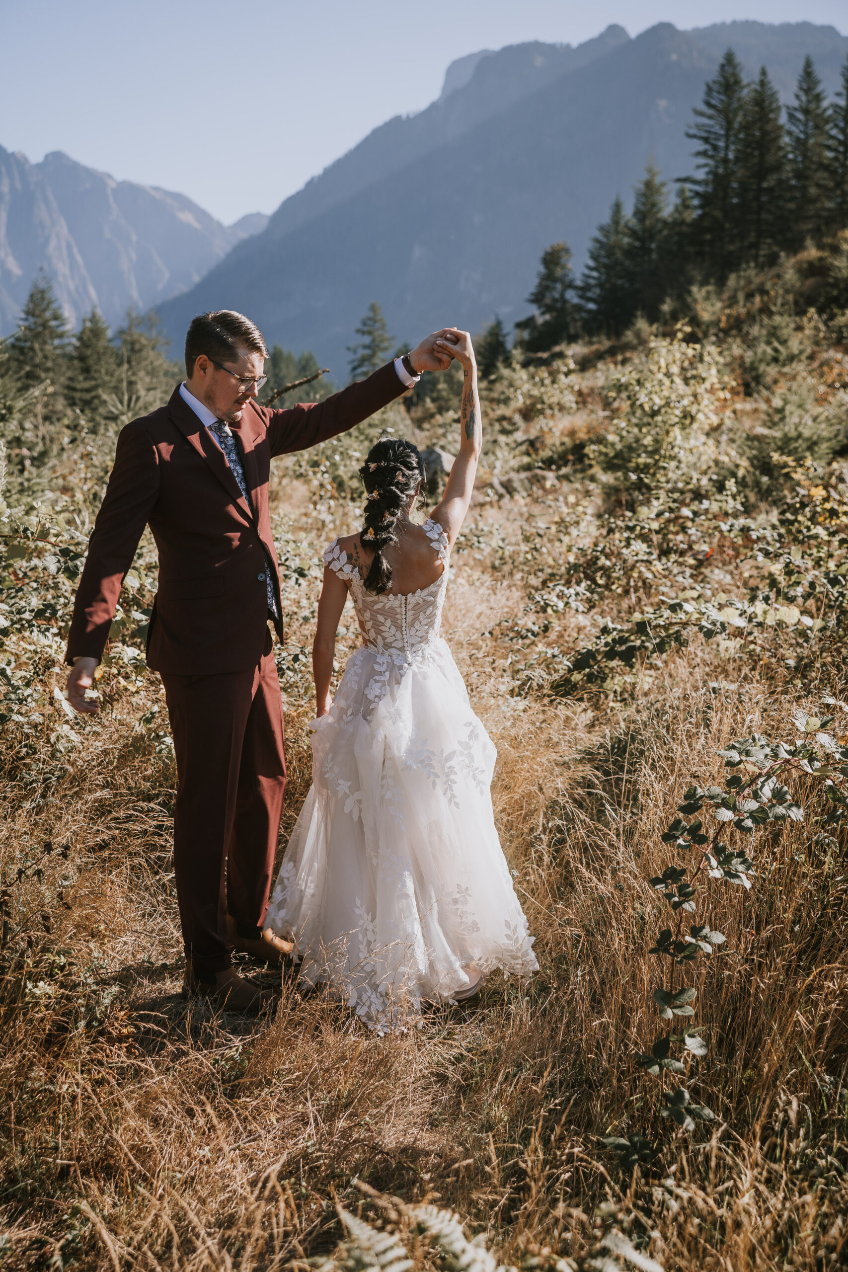 Brandon turning Morgan under his arm in the dry meadow grass with mountains behind