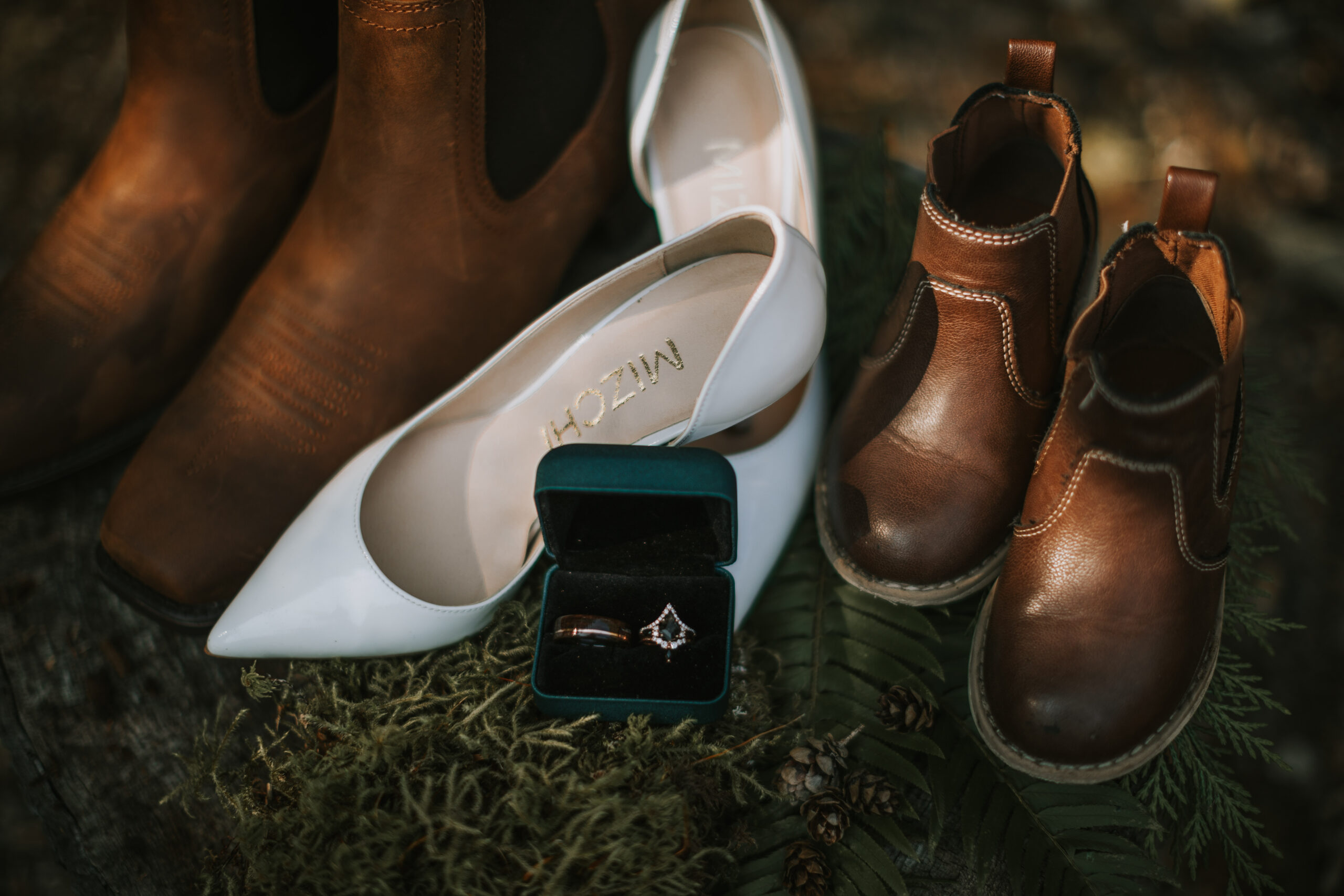 Detail of the bride's heels, the groom's boots and their son's boots around the ring box