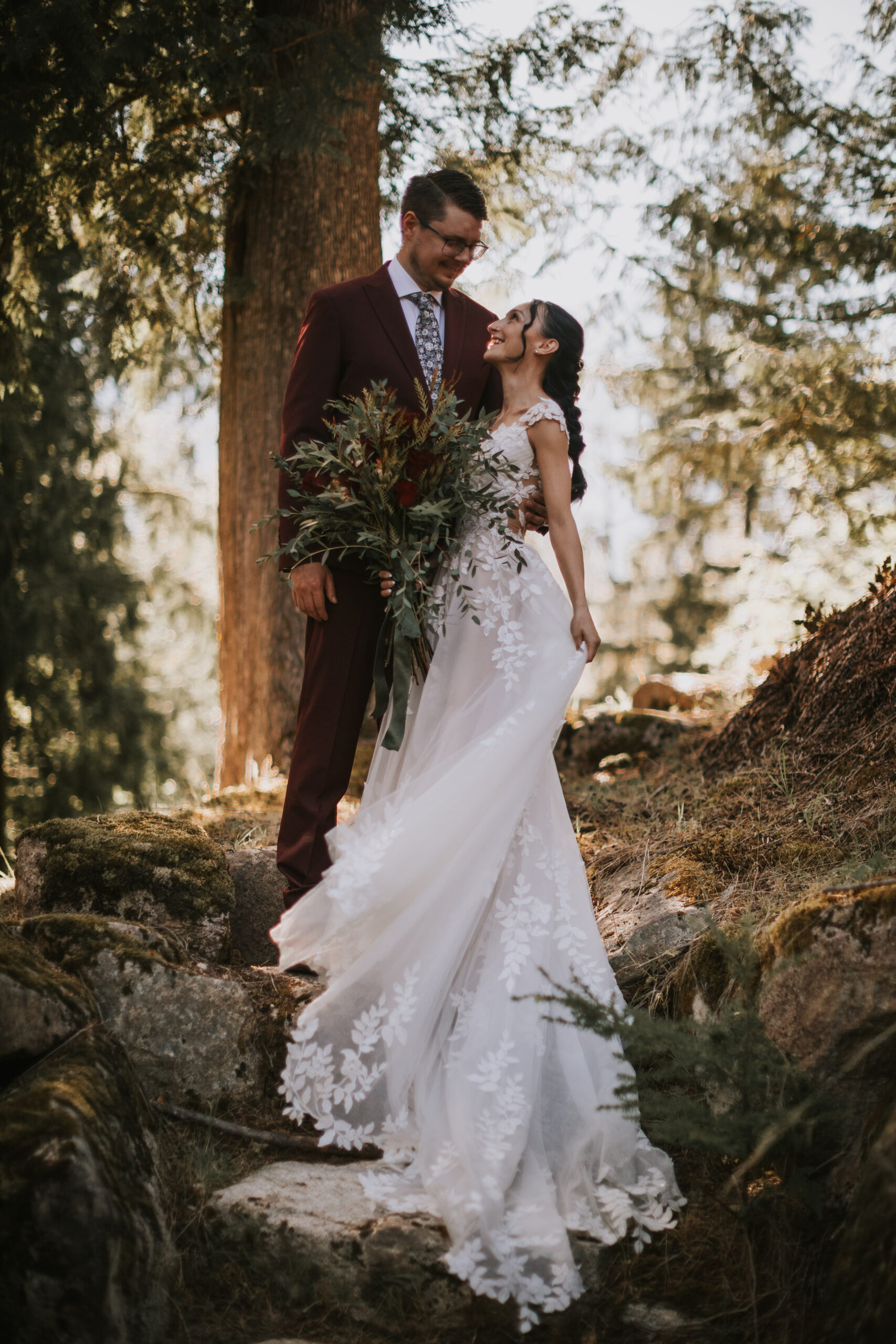 Brandon and Morgan laughing together in the forest, her bouquet across her arm