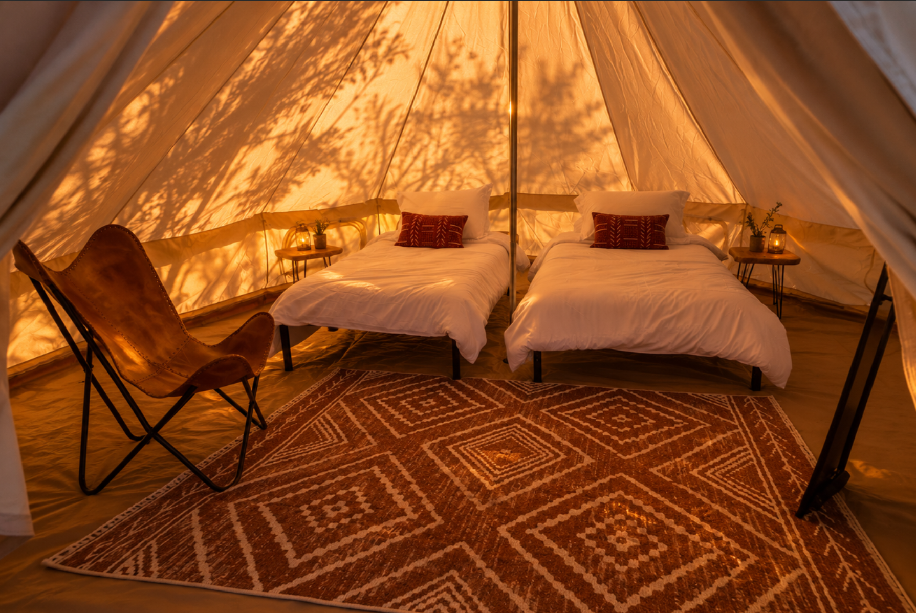 Inside a bell tent at That Desert Space, two twin beds made up with a patterned rug and a leather chair