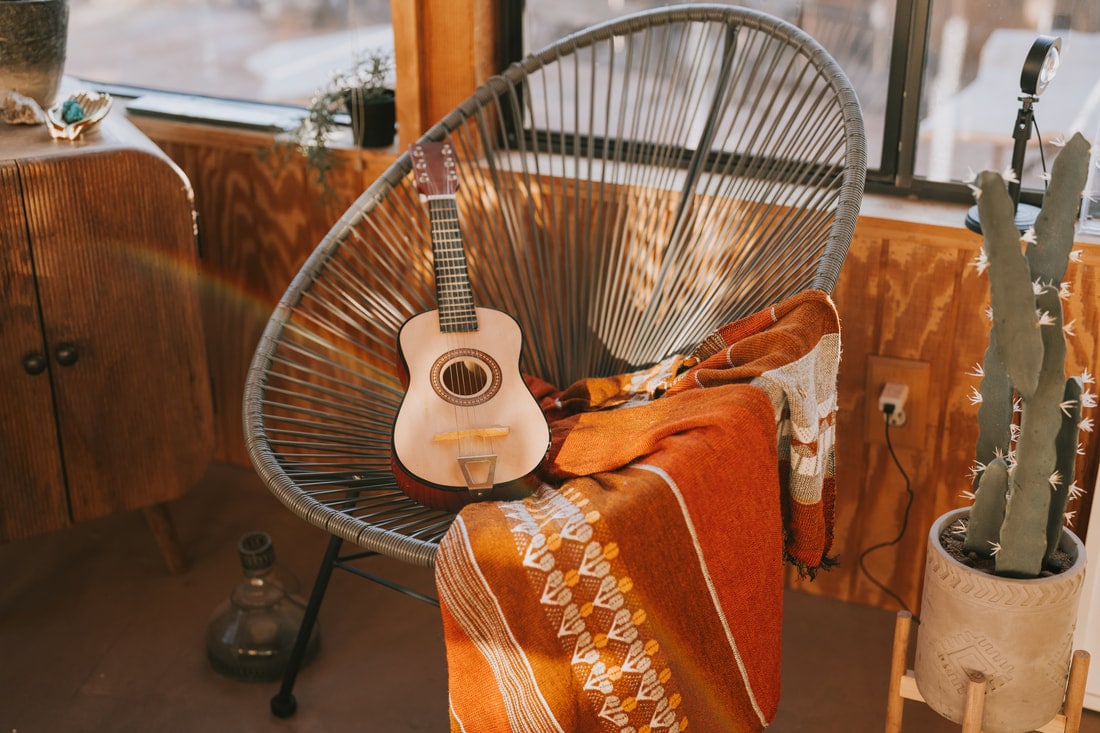 Inside That Desert Space, a guitar resting on a woven chair with a striped blanket and a potted cactus