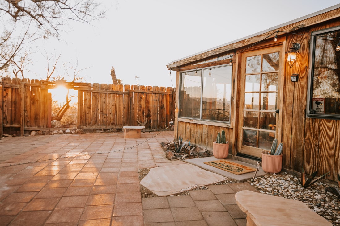 The fenced patio at That Desert Space at sunset, cactus in pots beside the door of the cedar house
