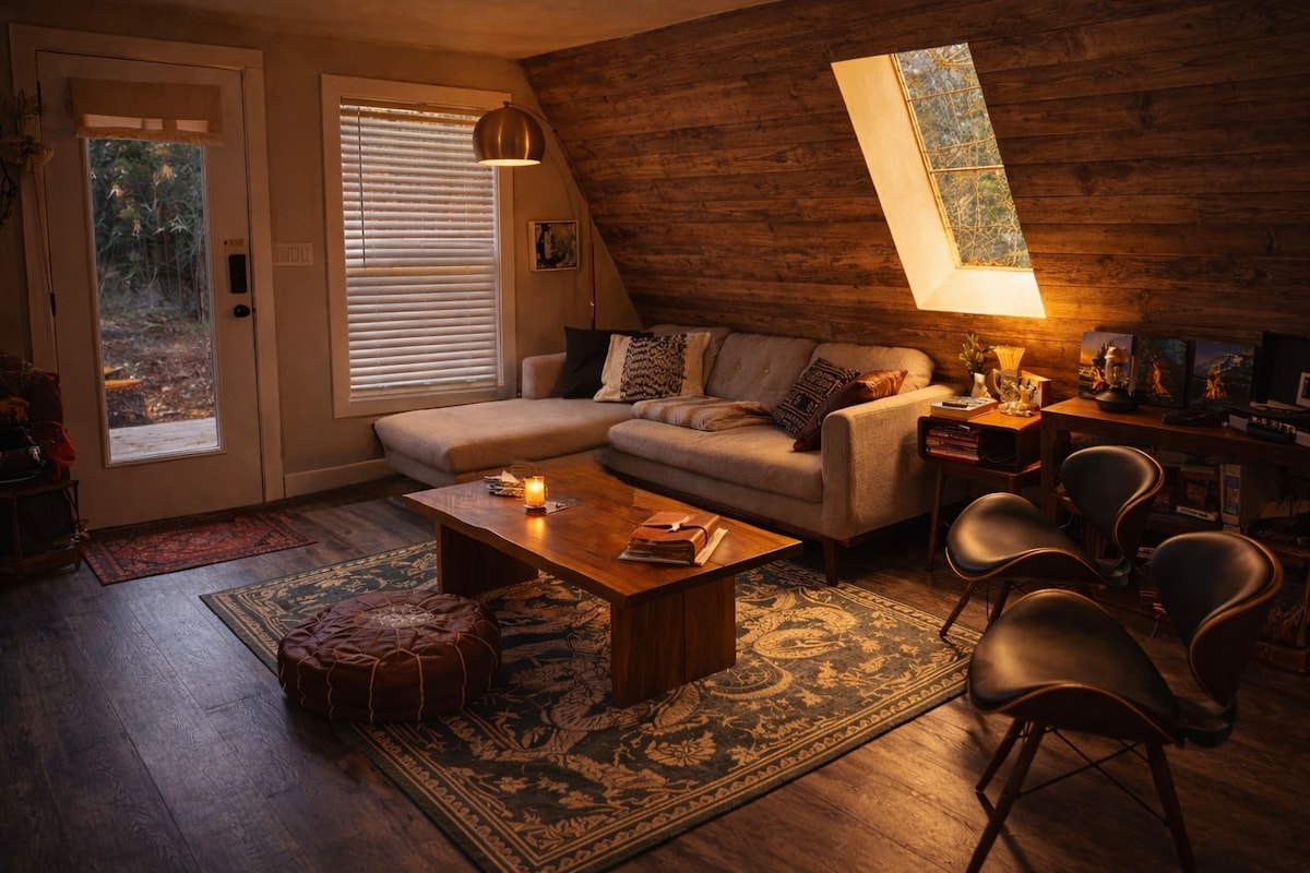 Inside That PNW Cabin, a sectional under the angled wall with a skylight, layered rugs and a low wooden table
